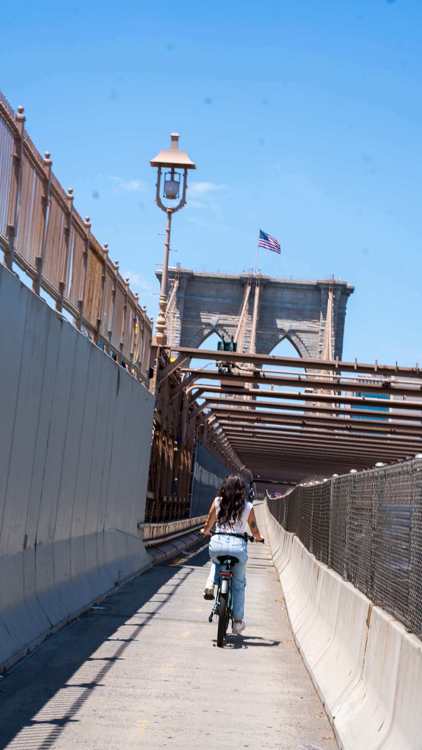 Customer riding a Velotric e-bike across the Brooklyn Bridge with American flag and gothic stone arches — historic NYC bike ride