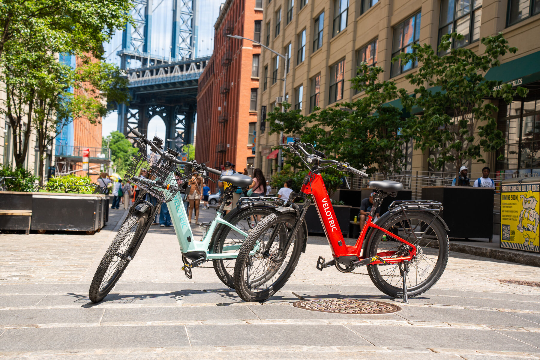 Velotric e-bikes on Washington Street DUMBO with Manhattan Bridge framed between Brooklyn warehouses — iconic NYC bike landmark